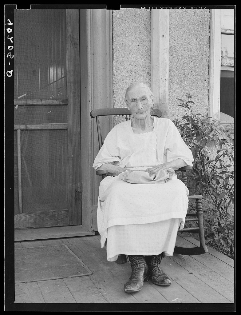 An elderly woman, Mrs. Springer, seated on the front porch of a Pennsylvania farmhouse in August 1938, photographed for the Farm Security Administration.