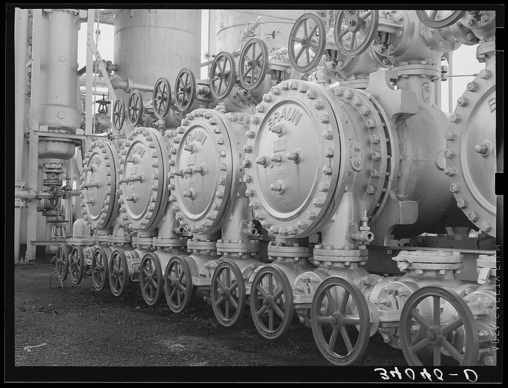 Stills and a bank of large hand-wheel valves on the pipework of an oil refinery at Seminole, Oklahoma, photographed in August 1939; the valves sit at the base of the stills with their connecting lines running overhead.