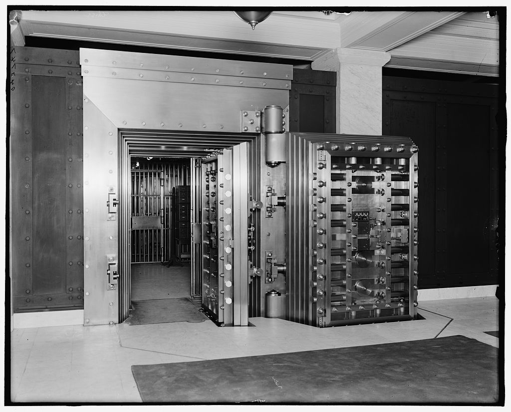 The massive round steel door of a bank safe-deposit vault, standing open on its hinges, photographed in Boston around 1913.