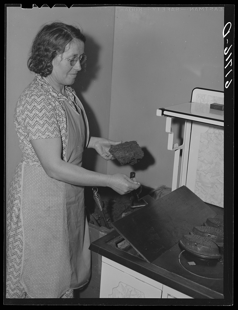 A farm woman feeding fuel into the kitchen stove in McIntosh County, North Dakota, in November 1940, photographed for the Farm Security Administration.