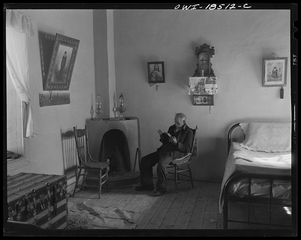Grandfather Romero, the oldest man in Trampas, New Mexico, at ninety-nine, seated alone in a room and reading, photographed in January 1943 by John Collier Jr. for the Office of War Information.