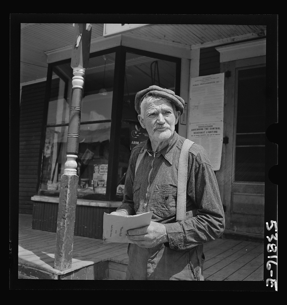 Frank Goss, a seventy-one-year-old Vermont farmer, standing in front of a general store and post office in July 1942, reading his mail.